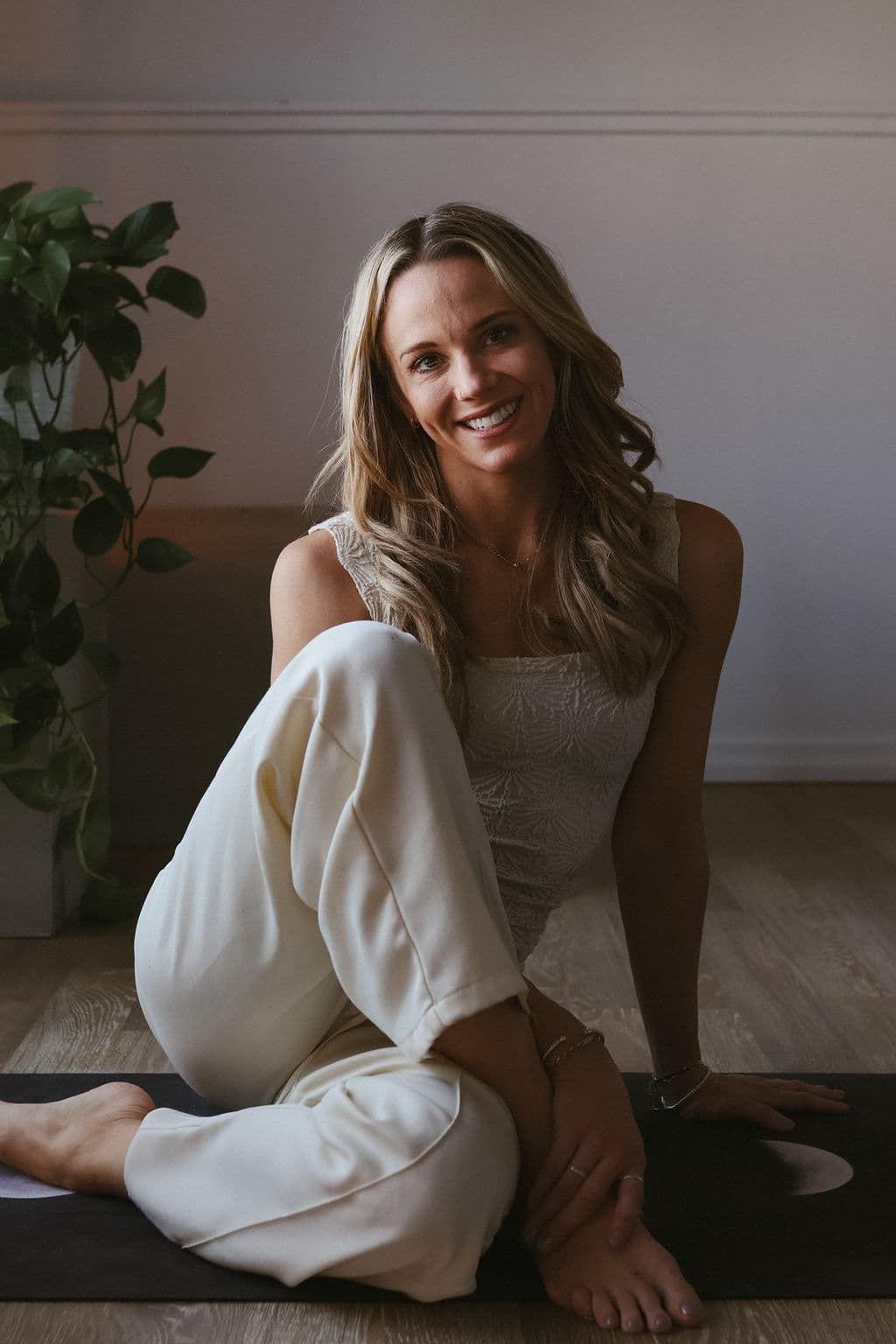 Nora L. Hollenkamp seated on a yoga mat beside a houseplant